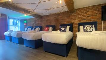 A hotel room with four beds arranged in a row, a brick wall, and a wooden ceiling.