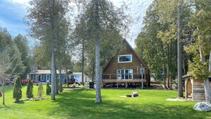 A cabin with a deck, surrounded by trees and a grassy yard. - The Aframe Beach front cottage rental on Manitoulin Island (Sheguiandah)