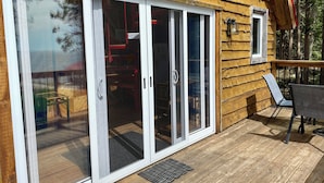 A wooden cabin with large sliding glass doors, a deck, and outdoor furniture. - The Aframe Beach front cottage rental on Manitoulin Island (Sheguiandah)
