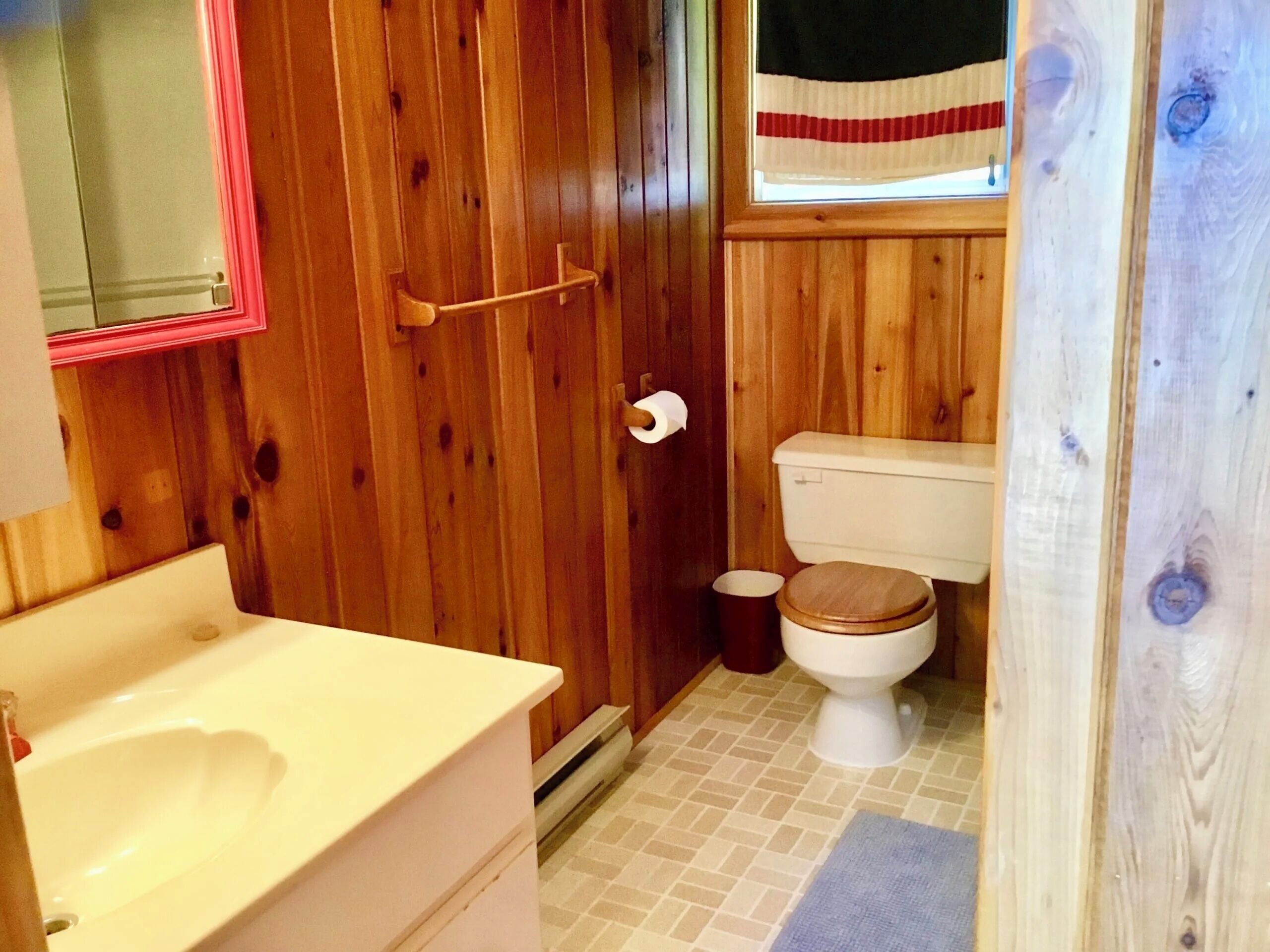 Une salle de bain aux murs lambrissés, avec un lavabo blanc, des toilettes et une porte en bois.
