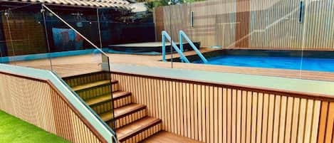 A swimming pool with wooden steps and a glass enclosure.