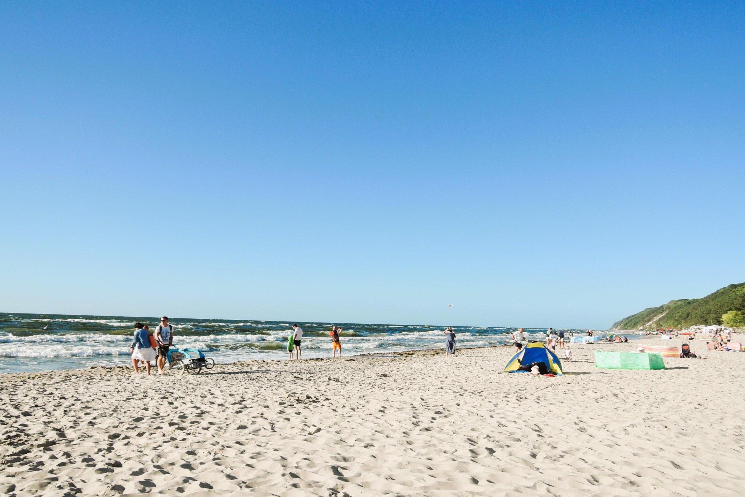 A sandy beach with people, a tent, and a clear sky.