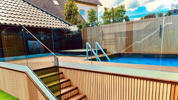 Uma piscina moderna ao ar livre com escadas de madeira e um revestimento de vidro.