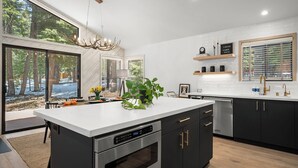A modern kitchen with a large island, built-in appliances, and a view of the forest.