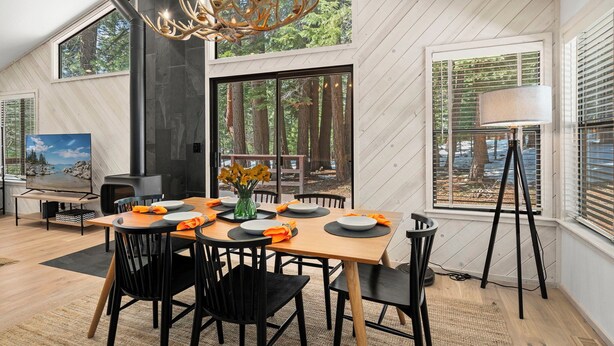 A modern dining area with a wooden table, black chairs, and a chandelier.
