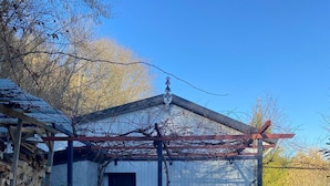 Un edificio rustico con una porta in legno, un portico coperto e una pila di legna da ardere.