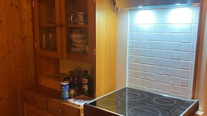 Una cucina compatta con piano cottura integrato, mobili in legno e una finestra con persiane a griglia.