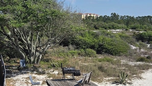 Une plage de sable avec une terrasse en bois, un barbecue et un banc.