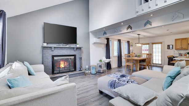 A modern living room with a fireplace, a flat-screen TV, and a dining area with wooden furniture. - Spacious & Charming Poconos Pine Hideaway (Tobyhanna)
