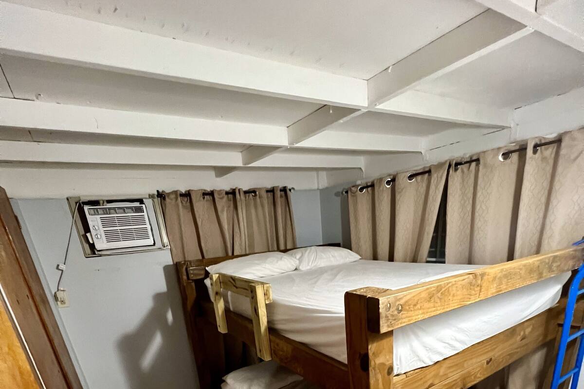 A bunk bed room with a ceiling fan, a window with curtains, and a door.