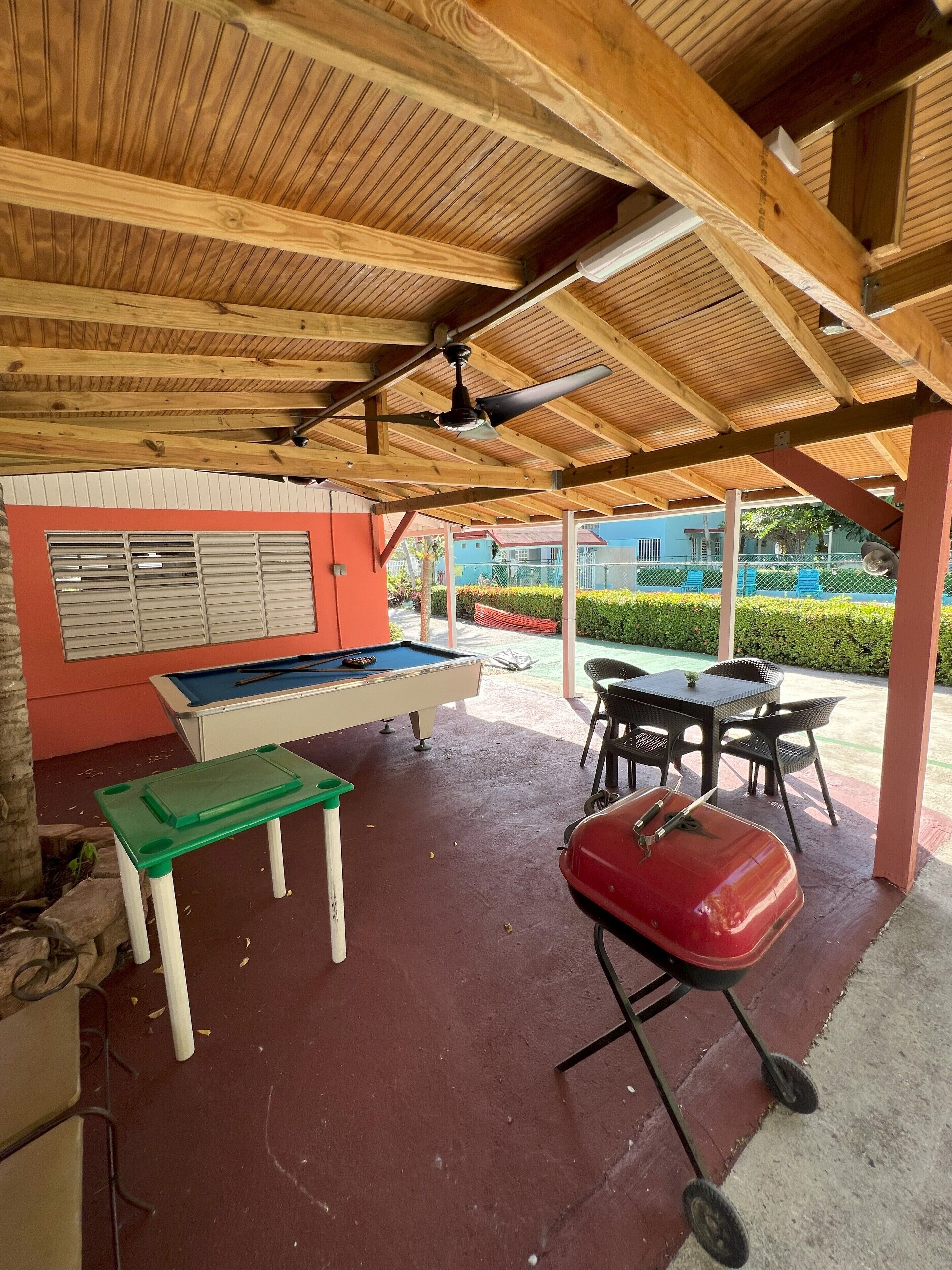An outdoor covered area with a pool table, a green table, and a red grill.