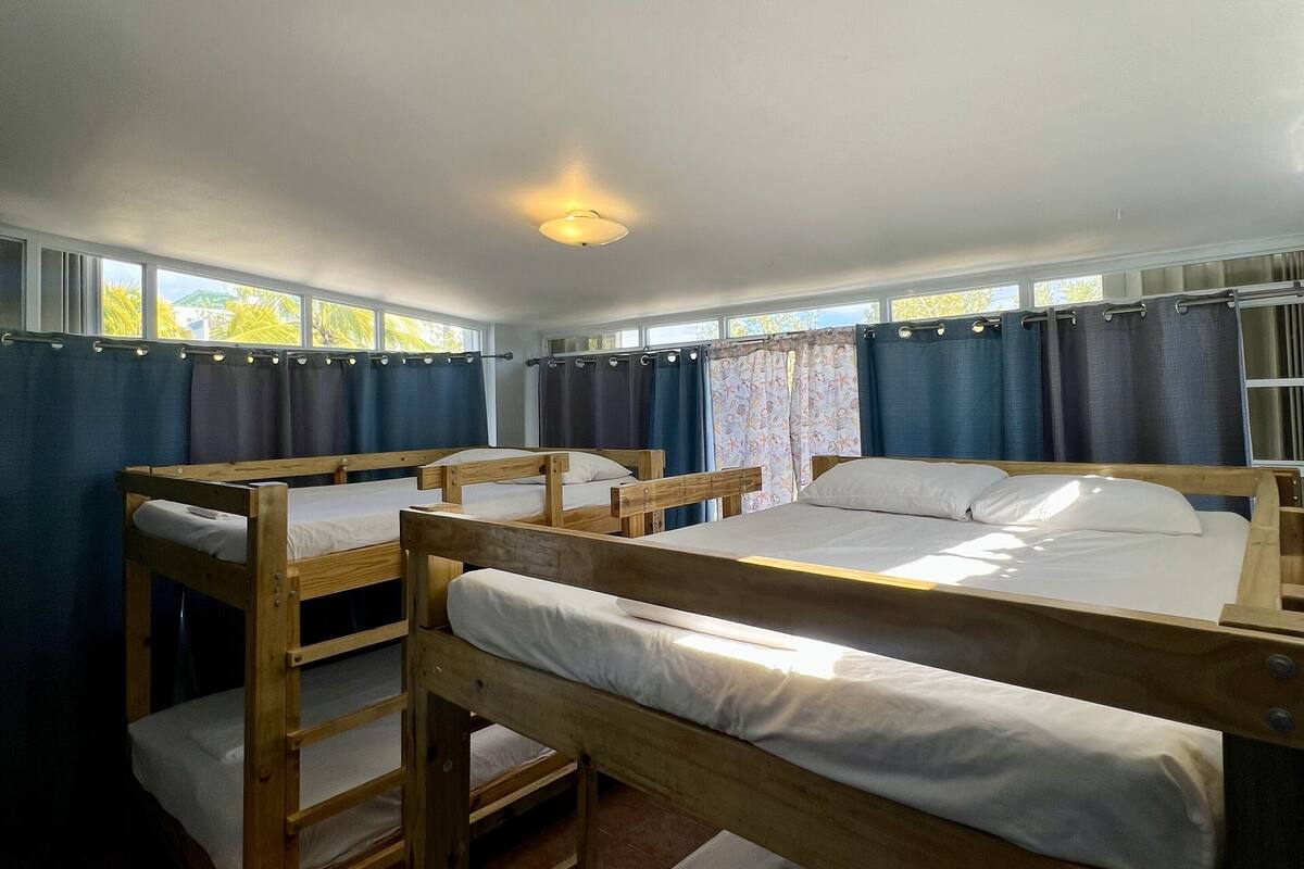 A dormitory room with bunk beds, a ceiling light, and windows with curtains.