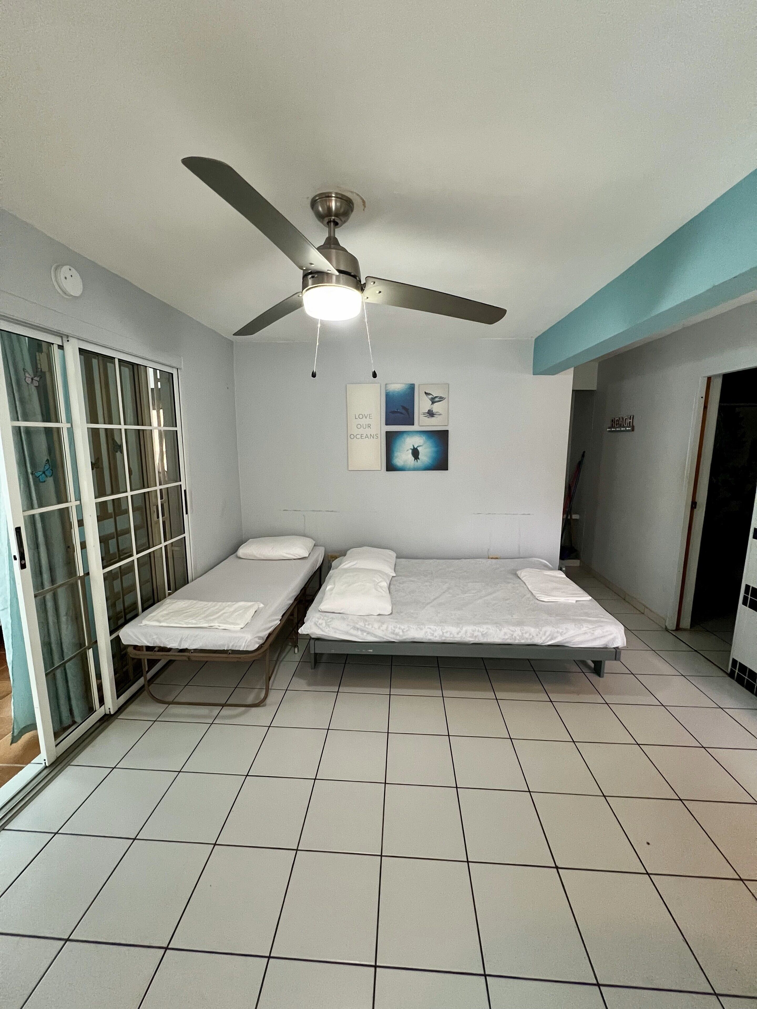 A room with two single beds, a ceiling fan, and a wall with ocean-themed artwork.