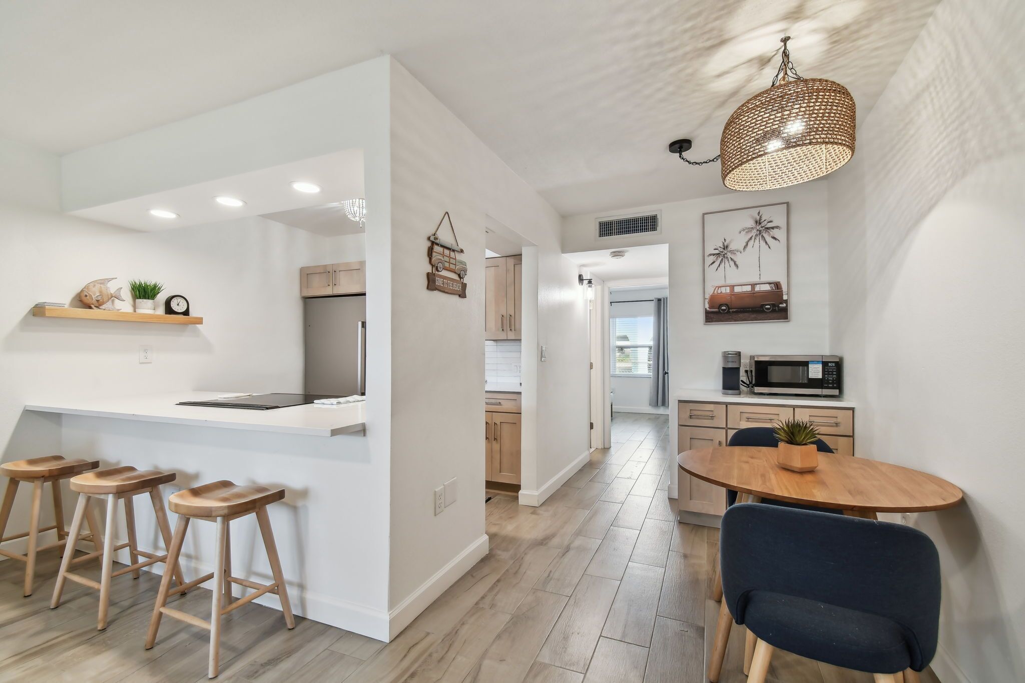 A modern kitchen with a central island, wooden stools, a dining table with chairs, and a hanging light fixture.