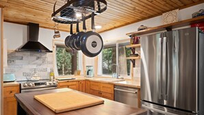 A modern kitchen with a wooden table, stainless steel appliances, and a large window.