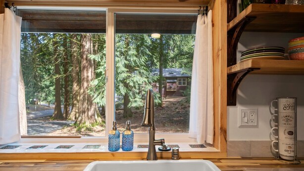A kitchen with a large window overlooking a forest, a sink, and a coffee station.