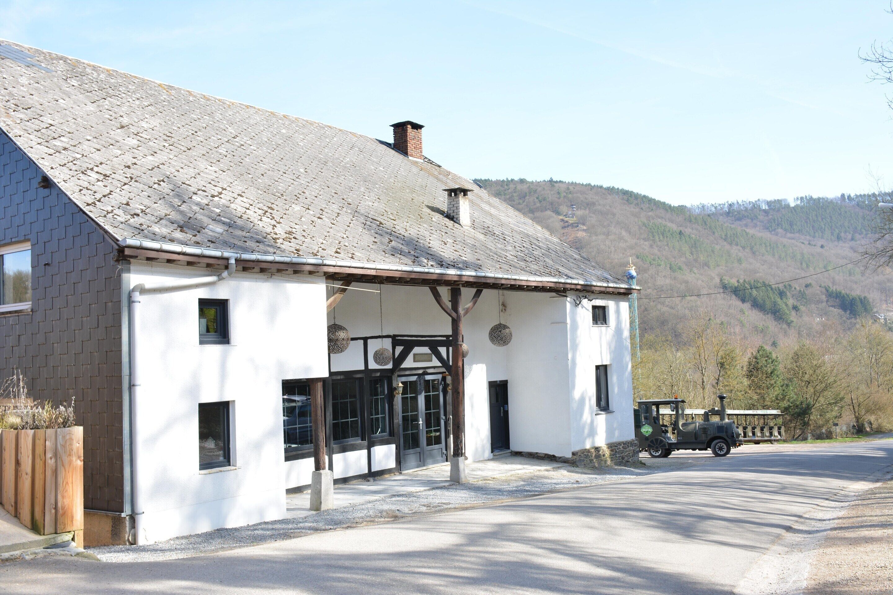 A white building with a sloped roof, a wooden porch, and a small train parked outside.