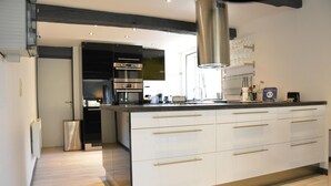 A modern kitchen with white cabinetry, stainless steel appliances, and a large island with multiple drawers. - Lake-view Apartment With Sauna, hot tub (Stavelot)