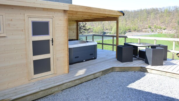 A wooden deck with a hot tub, outdoor furniture, and a view of a river and forest. - Lake-view Apartment With Sauna, hot tub (Stavelot)