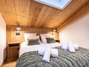 Une chambre confortable avec un plafond en bois, une lucarne, un grand lit avec une literie verte et deux tables de chevet avec des lampes.