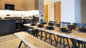A modern kitchen with wooden cabinets, a built-in microwave, and a dining area with a long table and stools. - Apartment in La Chapelle Near Ski Lift (La Chapelle-d'Abondance)