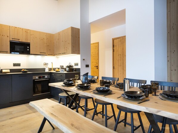 A modern kitchen with wooden cabinets, a built-in microwave, and a dining area with a long table and stools. - Apartment in La Chapelle Near Ski Lift (La Chapelle-d'Abondance)