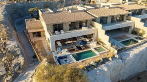 Uma casa moderna de vários andares com piscina, área de estar externa e paisagem rochosa.