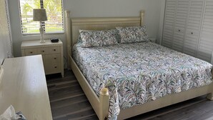 A bedroom with a bed, a ceiling fan, a window with blinds, a bedside table with a lamp, and a wardrobe.