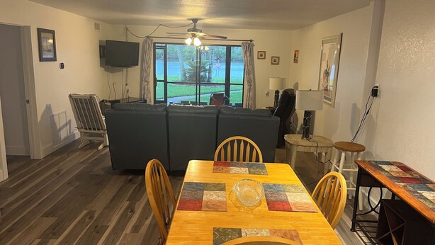 A dining area with a wooden table and chairs, a sofa, and a ceiling fan.
