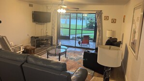 A living room with a leather sofa, a glass coffee table, a TV, and a ceiling fan.