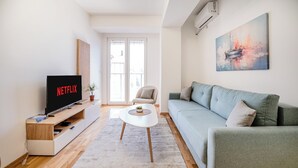Ein modernes Wohnzimmer mit Flachbildfernseher, einer Couch, einem Couchtisch und einem Bild an der Wand.
