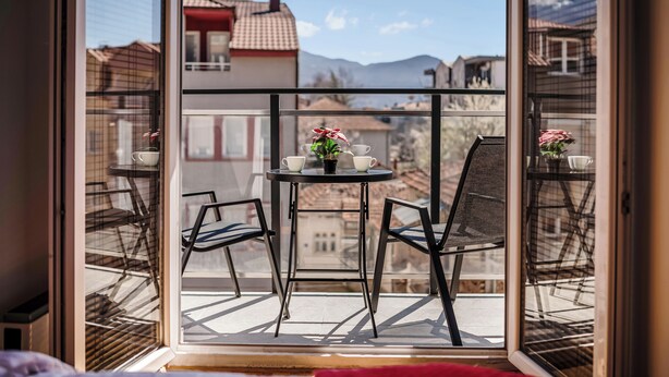 Ein Balkon mit Tisch und Stühlen, einem Blumentopf und Blick auf Gebäude und Berge.