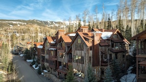 A multi-story lodge with a rustic wooden exterior, multiple balconies, and a ski slope in the background. - 10 Trails Edge-Curate Telluride, Ski-in/out, Walk to Gondola, Market, Hot Tub (Mountain Village)