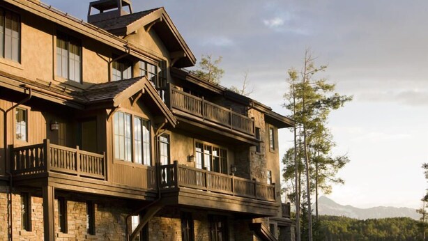 A multi-story stone building with balconies and large windows, set against a forest backdrop.