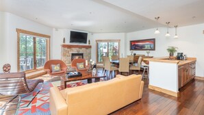 A spacious living room with a fireplace, a large TV, and a dining area with a kitchen island.