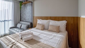 Habitación de hotel moderna con una cama grande, un sofá y vistas de la ciudad a través de cortinas translúcidas.