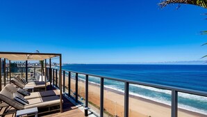 Een balkon met ligbedden met uitzicht op een strand en zee.