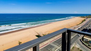 Uitzicht op een strand vanaf een balkon, met een weg en gebouwen op de achtergrond.