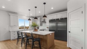 A modern kitchen with white cabinetry, a large island with bar stools, stainless steel appliances, and pendant lighting. - [The Grandview] Pool, Pickleball, Hot Tub, Views (Page)