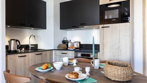 A modern kitchen with dark cabinets, a wooden dining table set for breakfast, and a Bosch microwave above the counter. - Apartment in Les Deux Alpes Near Ski Slopes (Les Deux Alpes)