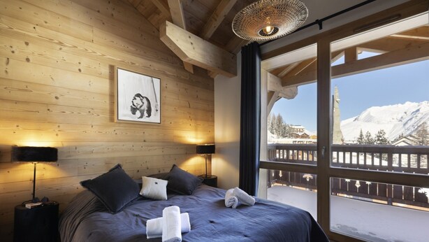 A bedroom with a large bed, two bedside lamps, a framed picture on the wall, and a view of a snowy mountain landscape through a balcony. - Apartment in Les Deux Alpes Near Ski Slopes (Les Deux Alpes)