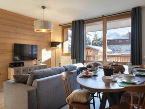 A cozy living room with a sofa, a dining table set with plates, cups, and a basket. A flat-screen TV is mounted on the wall, and there's a window with curtains. - Apartment in Les Deux Alpes Near Ski Slopes (Les Deux Alpes)
