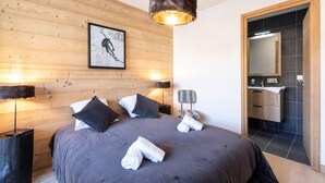 A bedroom with a large bed, wooden panel walls, a framed picture, bedside lamps, and a bathroom visible through an open door. - Apartment in Les Deux Alpes Near Ski Slopes (Les Deux Alpes)