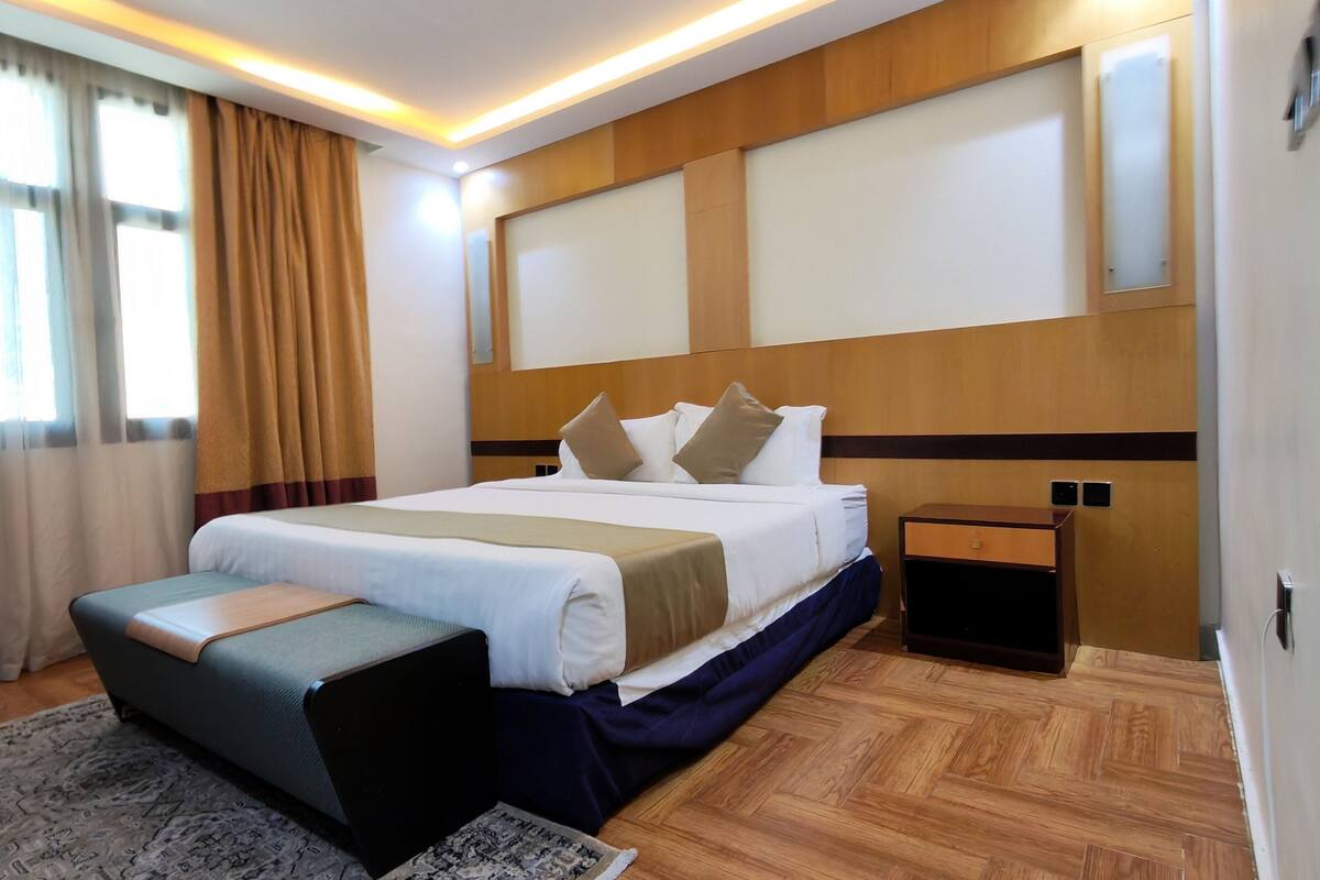 A hotel room with a large bed, a bedside table, a desk, and a window with curtains.