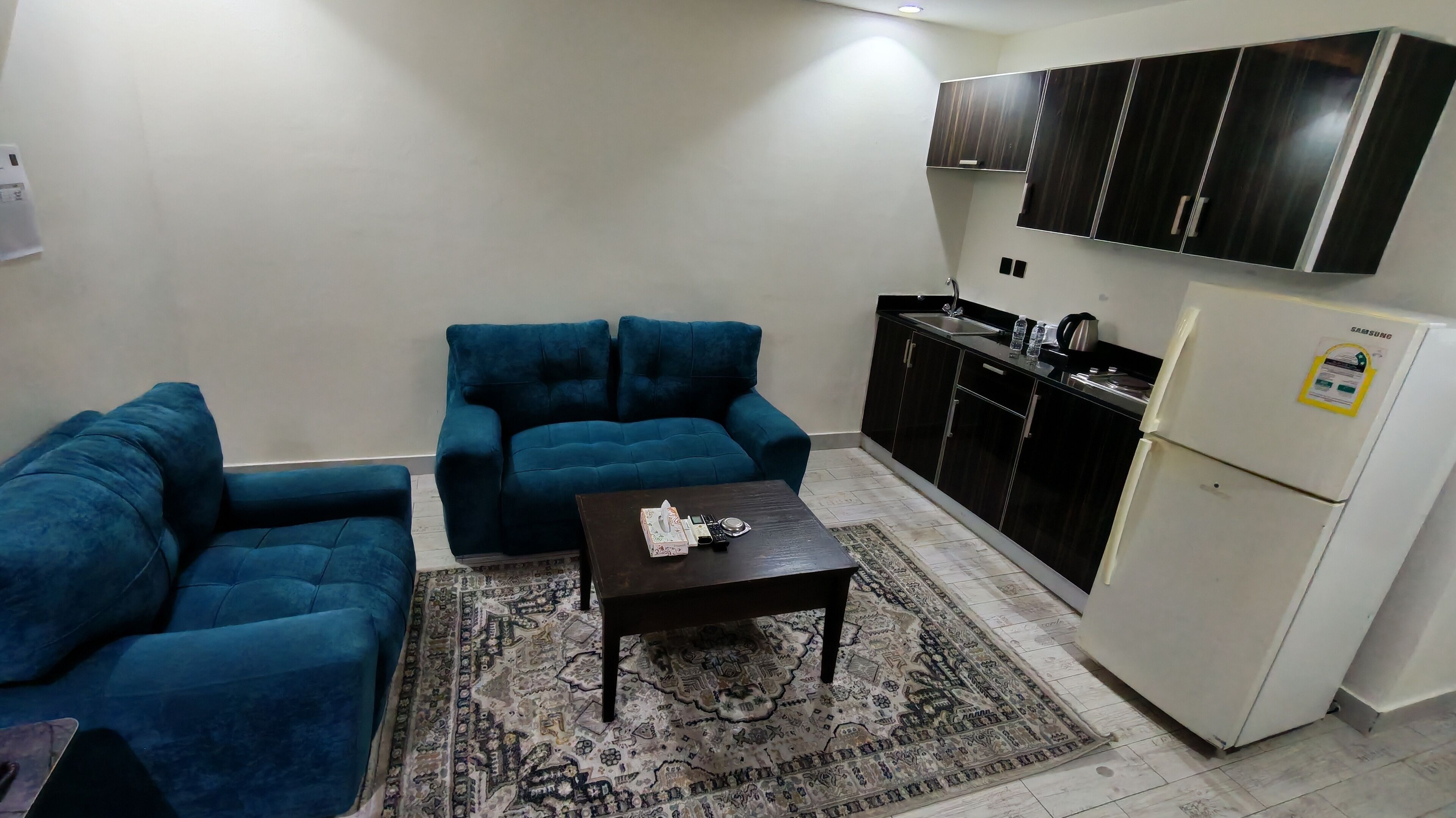 Un espacio habitable compacto con sofá, una mesita de centro y una zona de cocina que incluye armarios y un refrigerador.