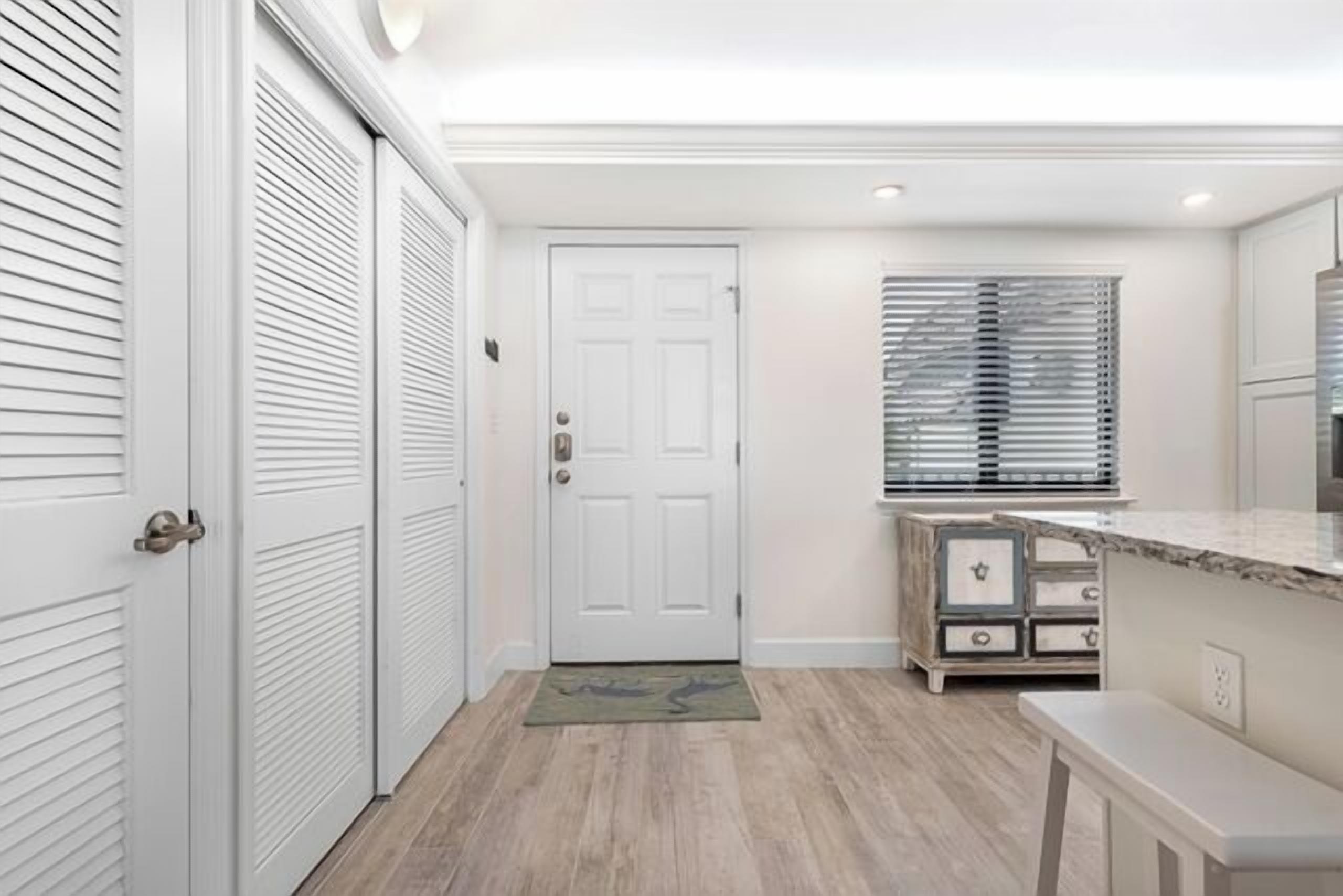 Un couloir avec une porte blanche, un banc et une petite table.