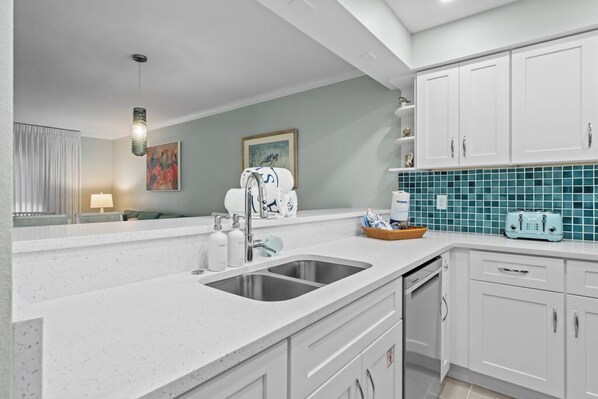 A modern kitchen with white cabinets, a double sink, and a teal backsplash.
