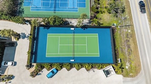 An aerial view of a tennis court with a pool, surrounded by greenery and a road.