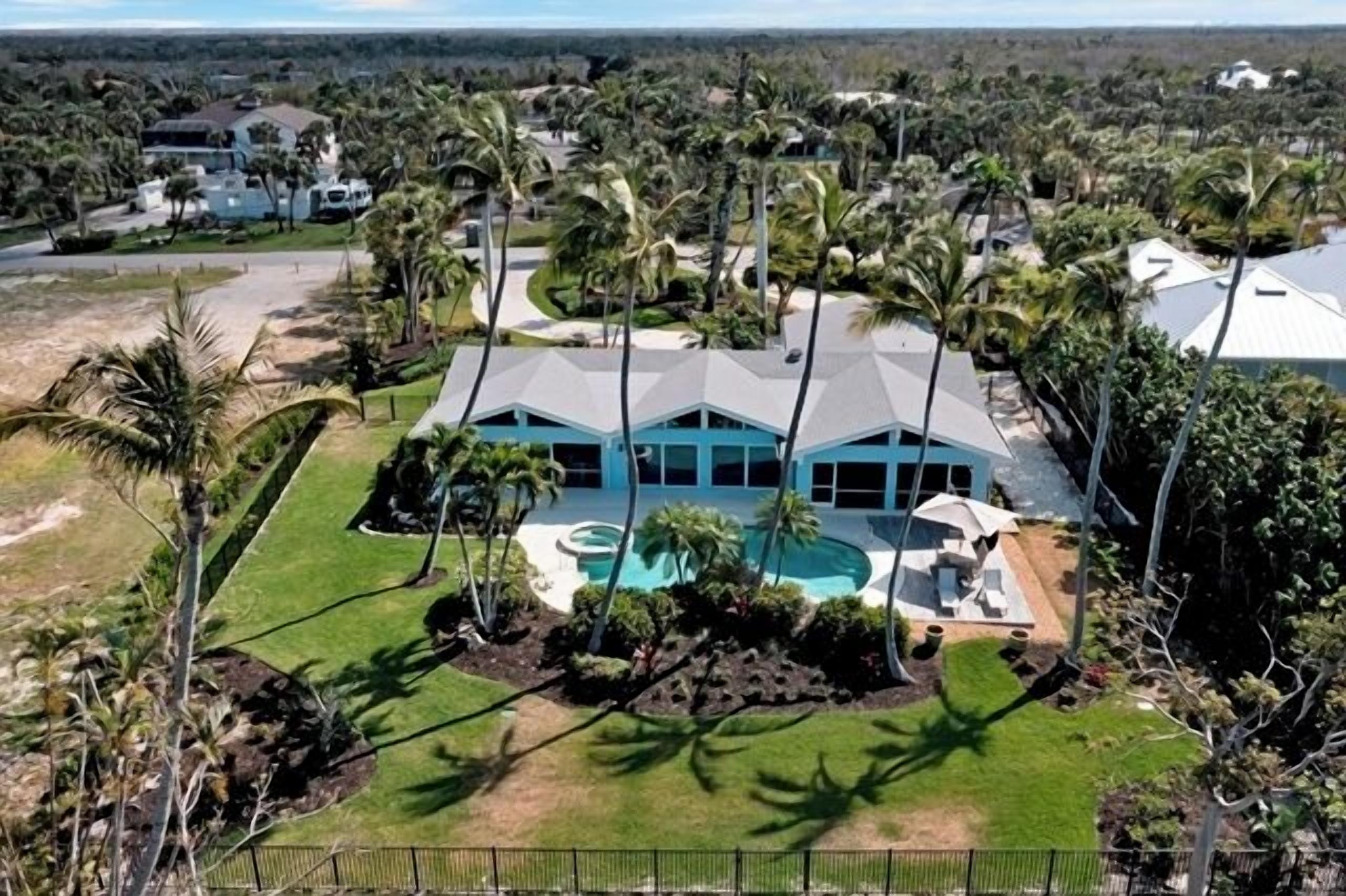 A large, modern house with a swimming pool, surrounded by palm trees and a well-maintained lawn.