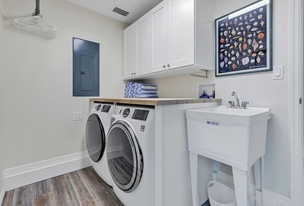 A laundry room with two front-loading washing machines, a sink, and a cabinet above the machines.